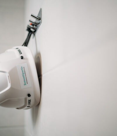 Kuvassa kylpyhuoneen seinän naulakosta roikkuva valkoinen suojakypärä. Kypärässä Remonttipartion logo.